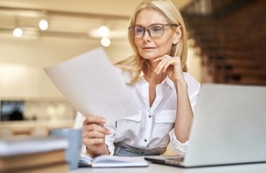 Woman behind laptop view a page she holds in hand